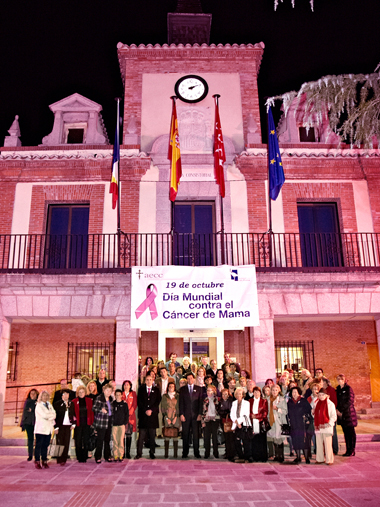 Los asistentes ante el ayuntamiento iluminado de rosa